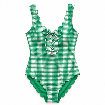 A green and white gingham one-piece swimsuit with scalloped edges, featuring a lace-up front detail with a silver heart-shaped charm.