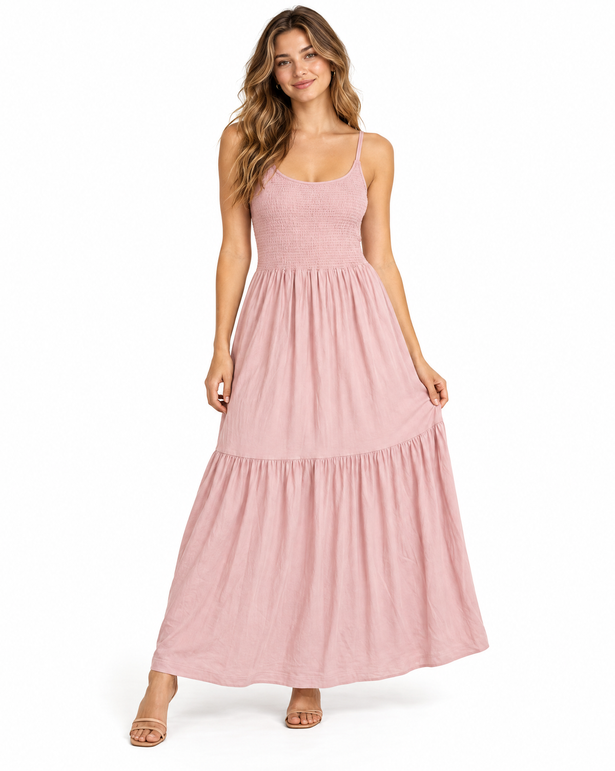 A woman modeling a dusty pink tiered maxi dress with thin spaghetti straps and a textured fabric, standing against a plain white studio background.