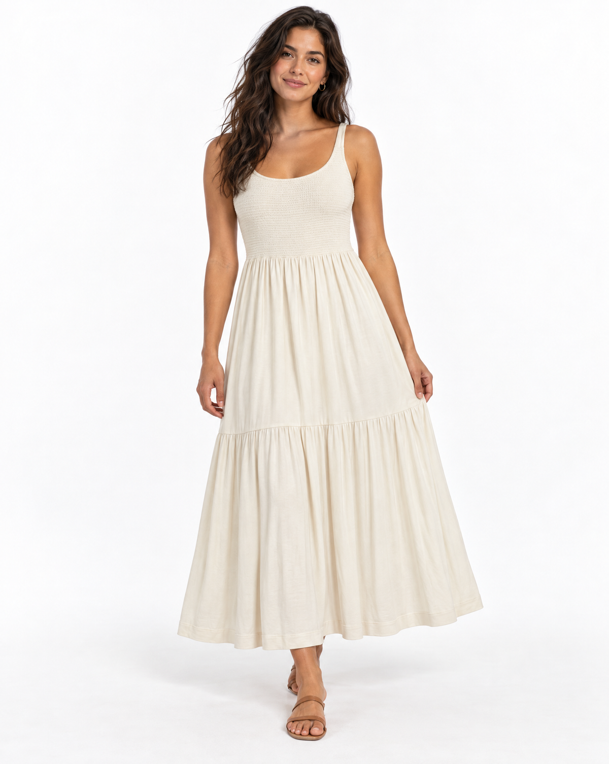 A woman modeling a sleeveless, tiered maxi dress in a warm off-white or cream color, standing against a plain white studio background.