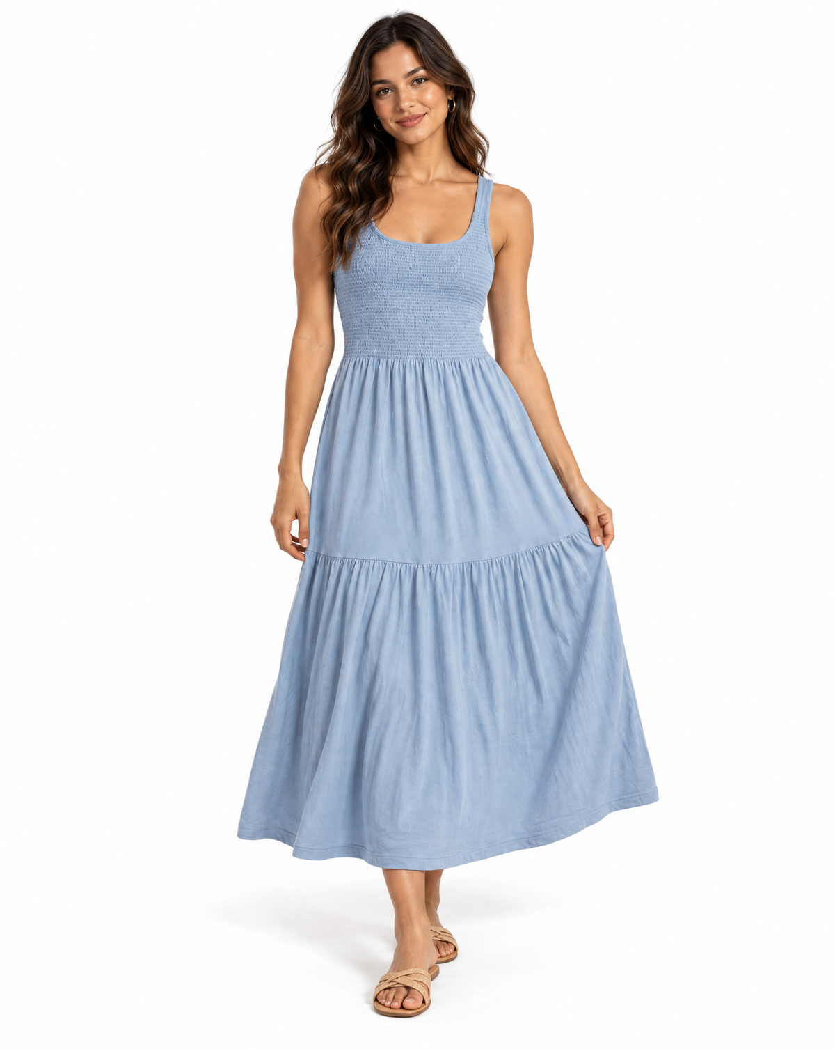 A woman modeling a light blue tiered maxi dress with a scoop neckline and thin shoulder straps, paired with tan flat sandals, against a plain white studio background.